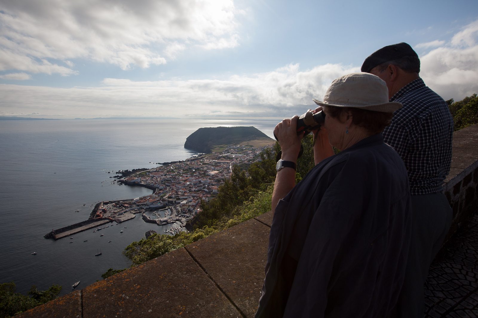 Duas pessoas a olhar pelos binóculos do miradouro sobre a vila de Velas e o Morro